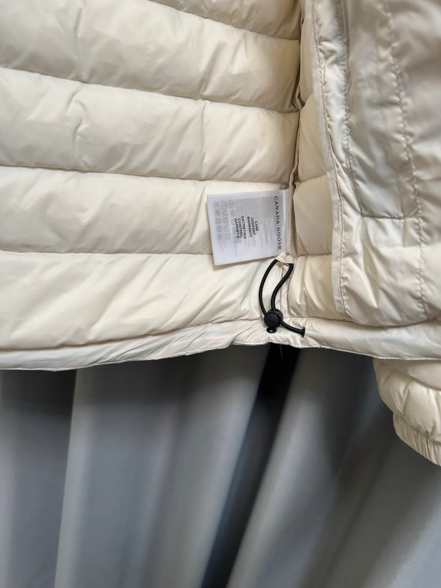 [Special grade down] 90% down Canada Goose/𝐂𝐚𝐧𝐚𝐝𝐚 𝐆𝐨𝐨𝐬𝐞 26FW red label lightweight hooded down jacket. Slim-fitting horizontal quilted version, neat and slim without being bloated. Classic round red label badge on the left arm, full of brand recognition. Integrated hood design, the hood is equipped with a drawstring adjustment buckle to tighten the hood to prevent wind. Fabric: The outer layer is made of high-density lightweight nylon fabric, which is thin and tear-resistant. It has water-repellent fabric to resist light rain and snow. The fabric is soft and not stiff, and can be stored and portable. The inside is filled with high-quality down, which is light and pressure-free, warm and stable, and there is no heavy burden on the upper body. Craftsmanship: horizontal strips are used to lock the down, and segmented quilting is used to firmly fix the down and prevent it from running away and clumping. The stitching is fine and smooth, each grid is evenly filled with velvet, and the pattern is long-lasting and not easy to collapse. The main zipper is smooth, the zipper webbing is printed with the brand logo, and the zipper closes tightly to lock in the internal temperature. Detailed workmanship: Built-in hand pockets on both sides, reinforced wiring, making it safer to place items. The cuffs are elasticated to prevent cold wind from entering. The hat rope is equipped with a Black plastic adjustment buckle, making it easy to adjust the tightness. The whole piece of clothing has fine hemming, clean thread processing, and neat tailoring, taking both practicality and texture into account. Color: Cream White Size: L/XL/2XL/3XL/4XL